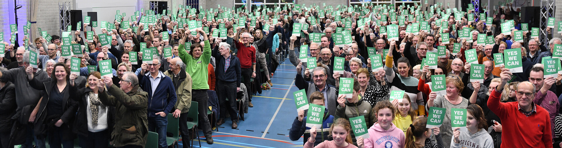 Langenbomers steken samen hun groene YES WE CAN-kaartjes omhoog tijdens een dorpsbijeenkomst